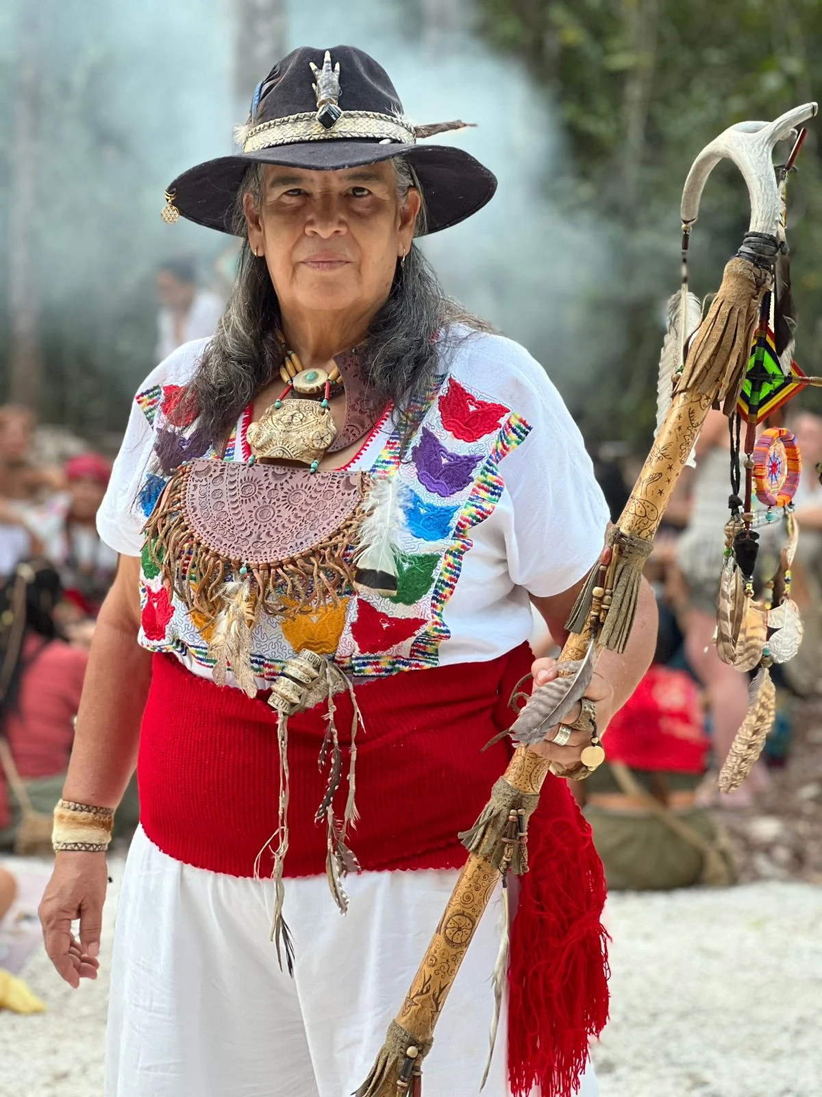 Abuela Martha Pico wearing a hat and embroidered clothing, holding a ceremonial staff
